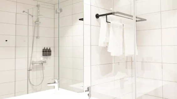 Valoisa ja toimiva kylpyhuone, jossa on kaakeloitu suihkutila, tyylikäs pesuallas ja siististi ripustetut valkoiset pyyhkeet.