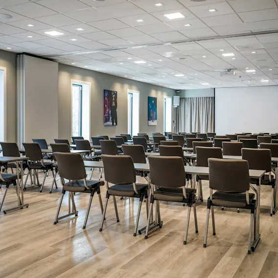 Et romslig, moderne konferanserom med rader av bord og stoler, klart for et møte eller en presentasjon.