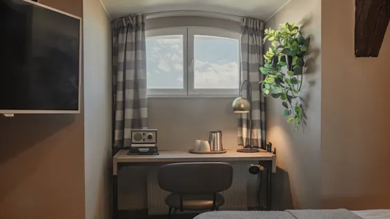 A comfortable hotel room with a dedicated workspace by a window, featuring a desk, chair, and a book titled VINNARNA.