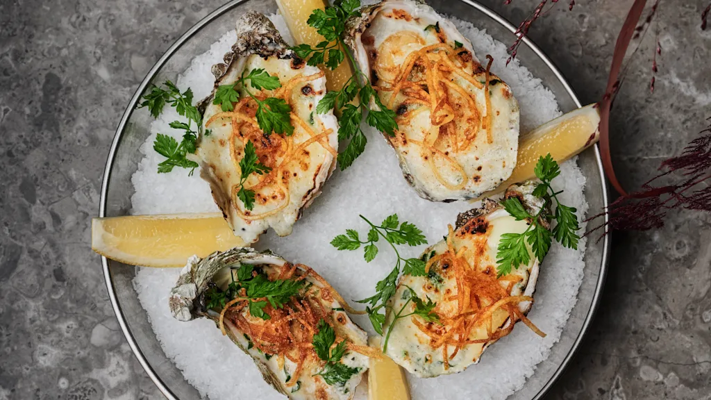 En gourmetrett med gratinerte østers pyntet med friske urter og sprø topping, servert på en seng av salt med sitron.