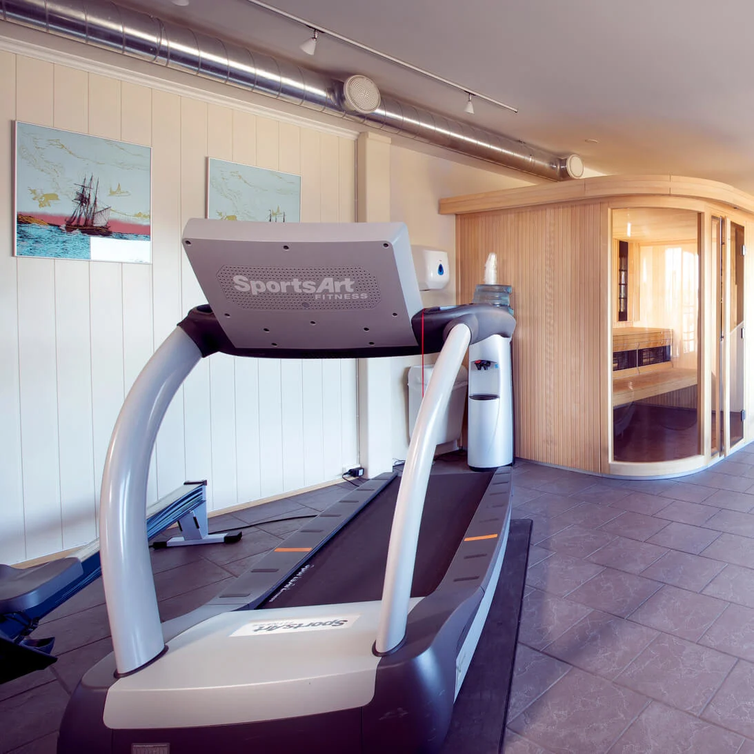 Ett löpband, bastu och träningscyklar i ett välbelyst, rymligt inomhusgym.