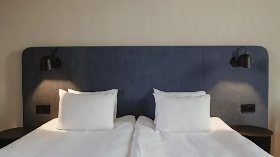 A cozy hotel room at Home Hotel Tapetfabriken with two beds, white linens, a blue headboard, and warm lighting.