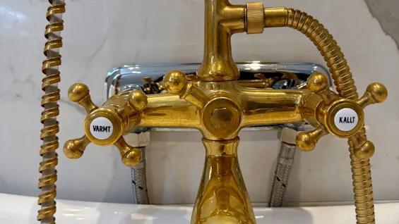 Kultainen vintage-kylpyammehana suihkupäällä, merkitty VARMT ja KALLT. Junior sviitti Comfort Hotel Linköping Cityssä.