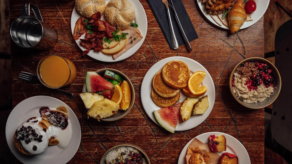 En varierad frukostbuffé utspridd på ett träbord, vilket antyder en gemensam måltid.