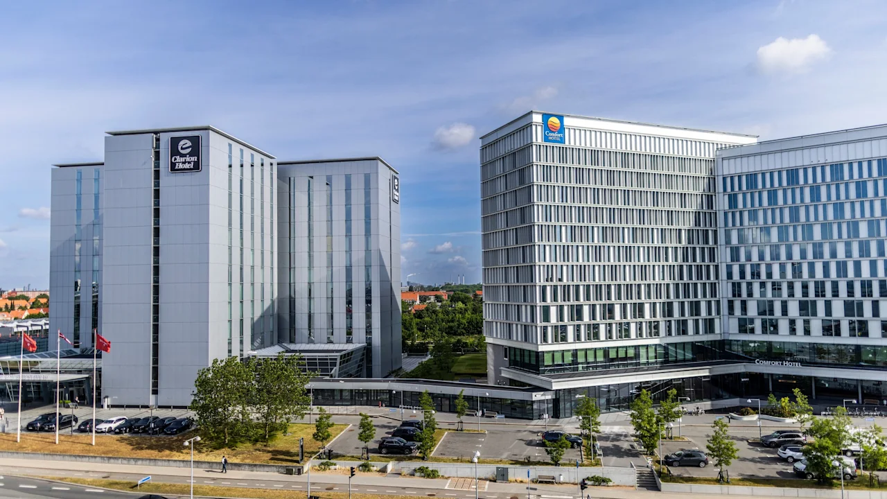 To moderne hotellbygninger under en blå himmel, med en vei og parkeringsplass. En bygning har 'Hotel' synlig, den andre har 'Hotel' ved inngangen.