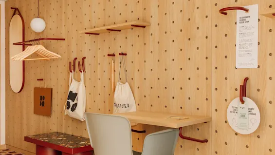 A versatile room at hobo oslo with a pegboard wall, desk, chair, and storage. Signs read: TO BORROW DURING YOUR STAY, CLEAN.