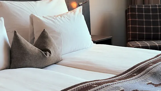 Mysigt hotellrum med en bäddad säng prydd med en mönstrad filt och en tänd sänglampa