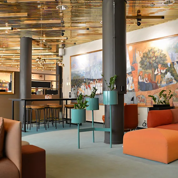 En modern hotellobby med färgglada soffor, gröna växtställ och en stor konstnärlig väggmålning