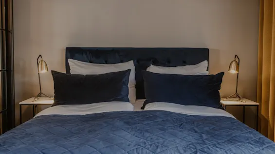 Ett mysigt hotellsovrum med en stor säng, blå sängkläder och två sänglampor, redo för en bekväm vistelse.