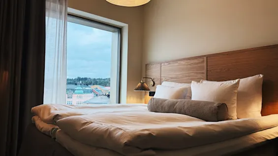 Ett mysigt hotellrum med en bäddad säng och ett stort fönster med utsikt över staden.