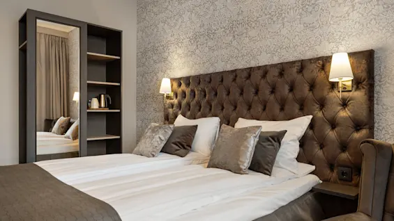 Et komfortabelt hotelværelse med en stor seng, elegant tuftet sengegavl og et klædeskab med spejl.