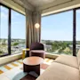 A modern hotel room with a comfortable sofa and armchair, featuring large windows that offer a panoramic view of the city.