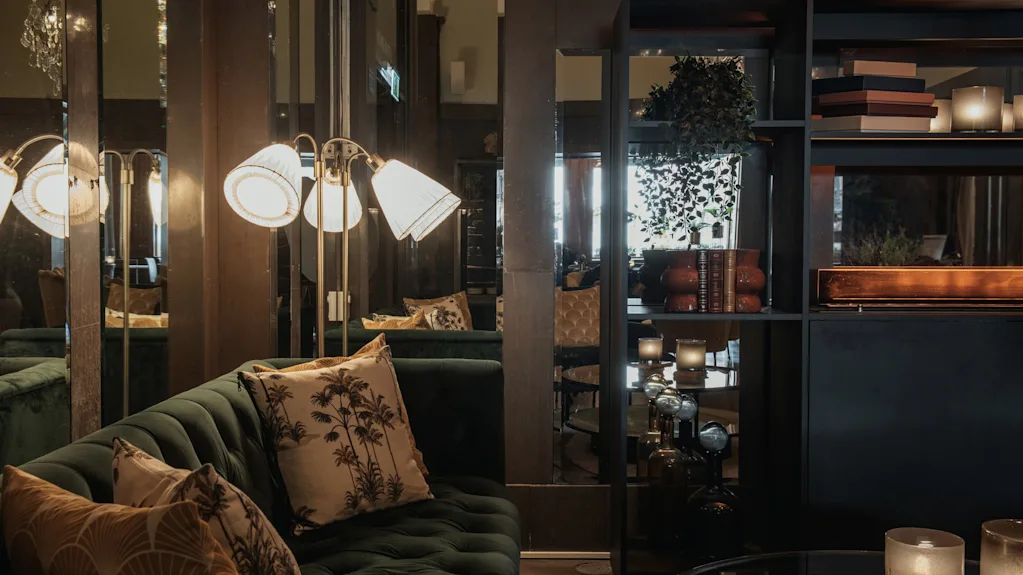 Inbjudande lounge på Home Hotel Grand, Helsingborg, med en plyschgrön soffa, varm belysning och elegant inredning för avkoppling.