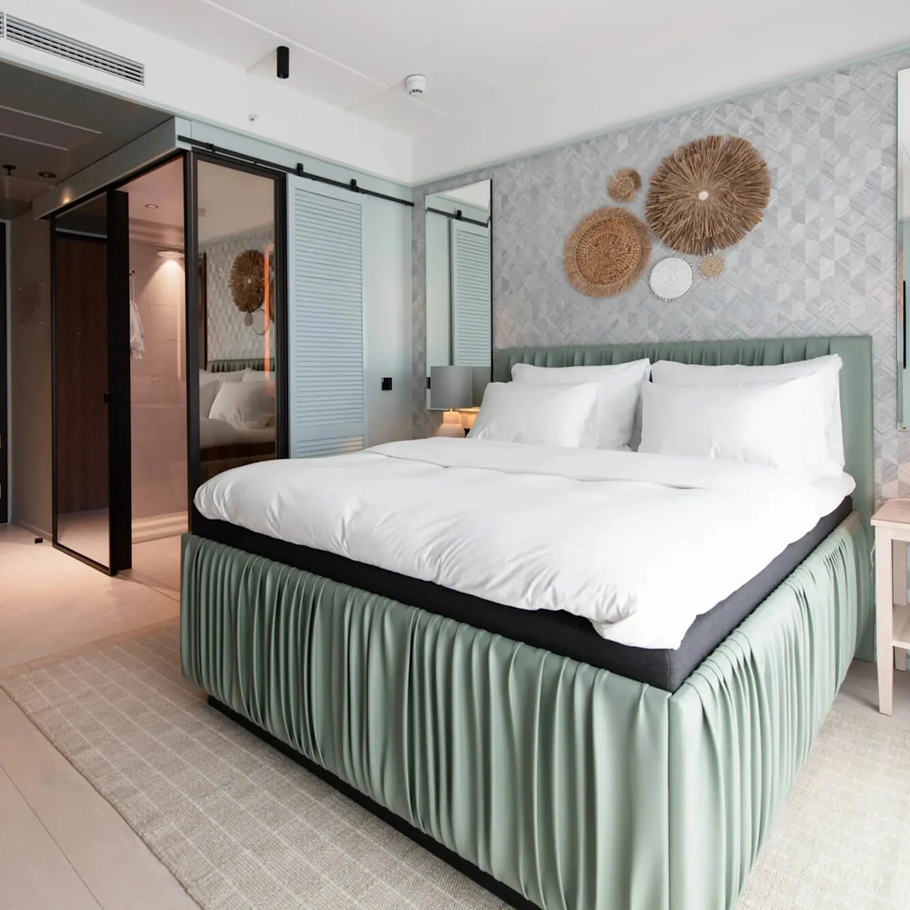 A bed with white linens stands in a modern hotel room; decorative wall art and a nightstand with a lamp add elegance.
