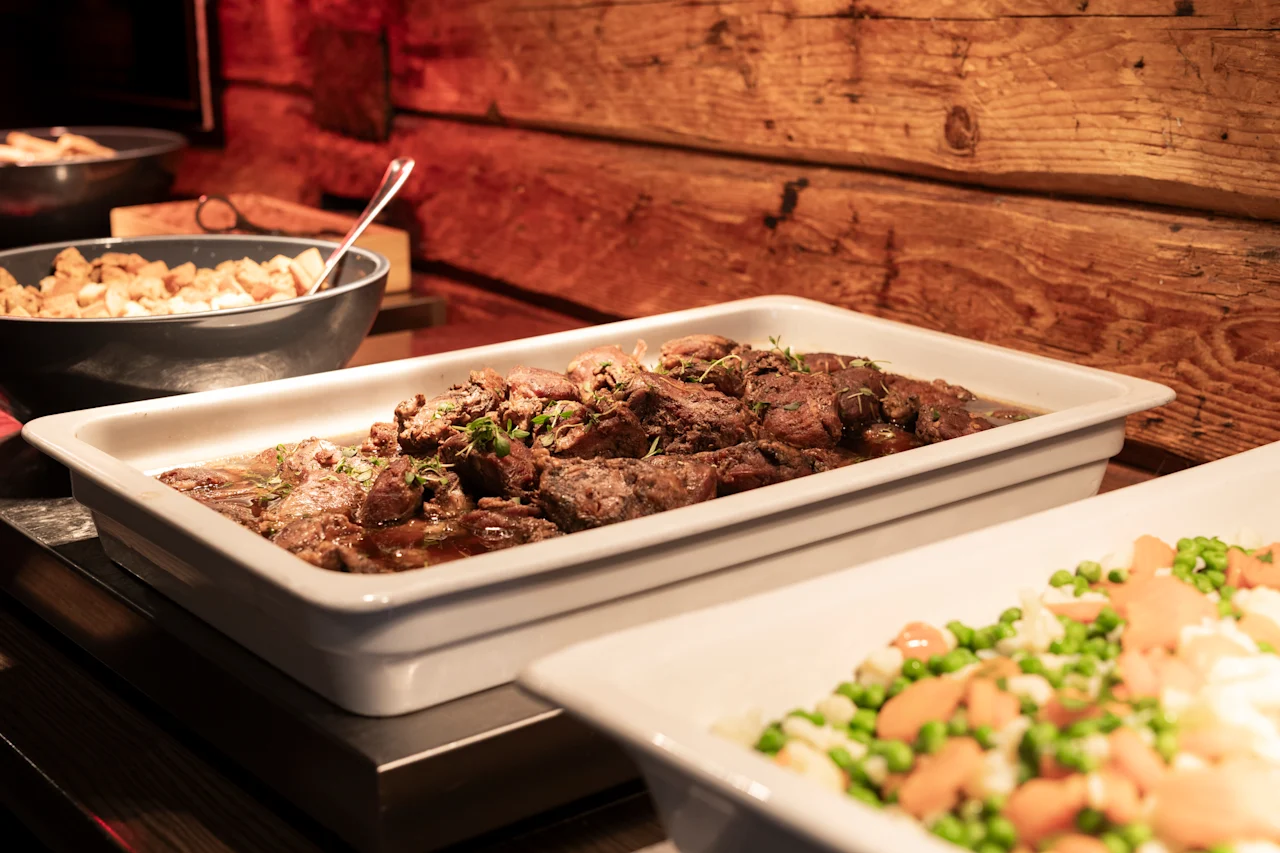 En lækker buffet med en hovedret af kød og en farverig sideret med blandede grøntsager, anrettet mod en rustik træbaggrund.