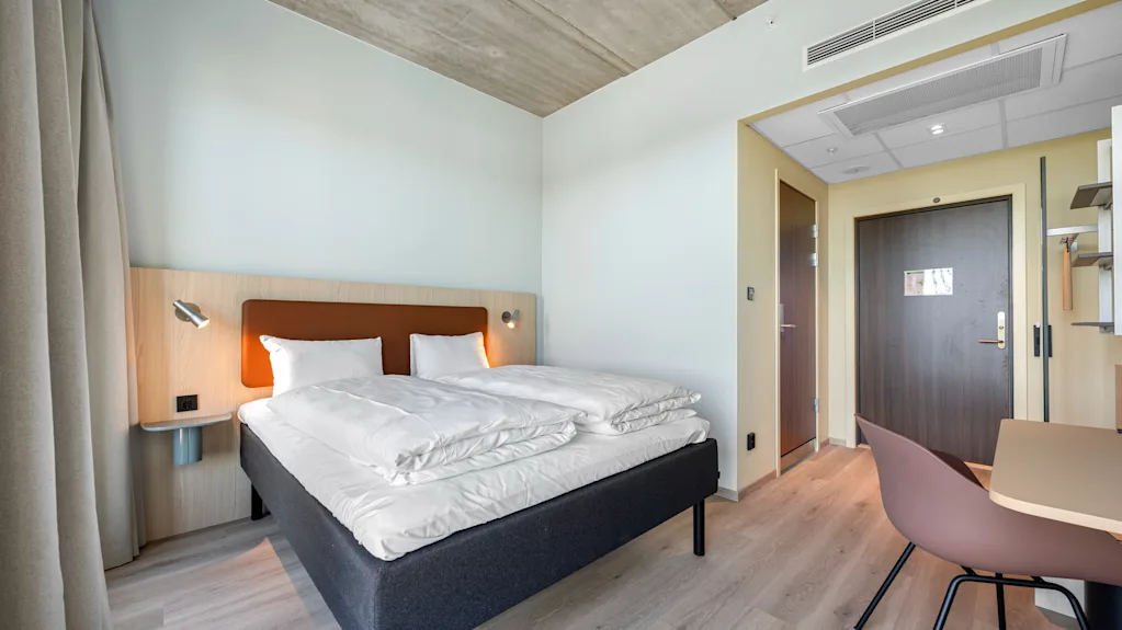 A modern and inviting hotel room with a comfortable bed, a small workspace, and warm lighting.