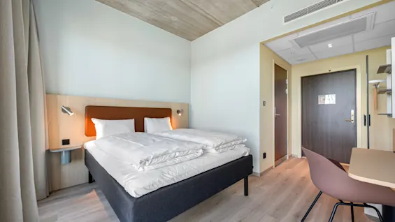 A modern and inviting hotel room with a comfortable bed, a small workspace, and warm lighting.
