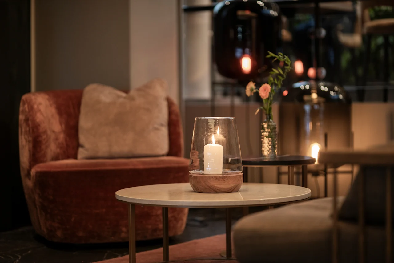 A cozy lounge area at Home Hotel Grand Bodø with a lit candle on a coffee table, an armchair, and flowers, creating a warm ambiance.