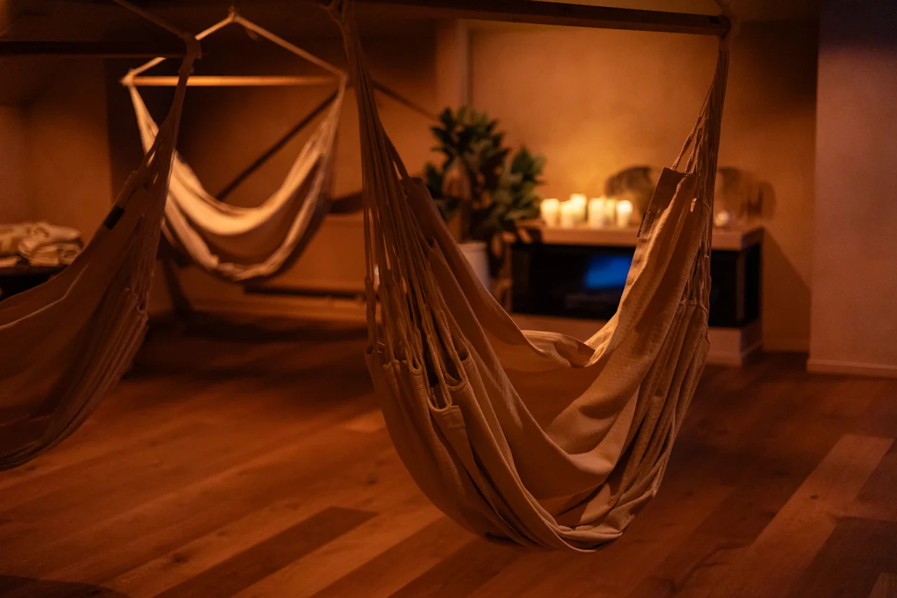 Viihtyisä huone, jossa on useita riippumattoja, valaistuna lämpimällä, himmeällä valaistuksella ja kynttilöillä, luoden rentouttavan tunnelman.