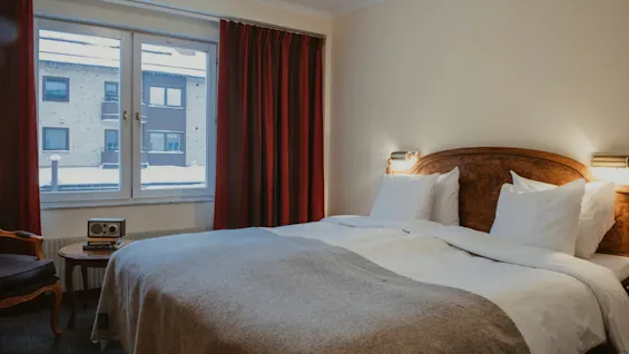 Ett mysigt hotellrum med en säng, ett fönster med utsikt över ett snöigt landskap och ett litet bord med en radio.