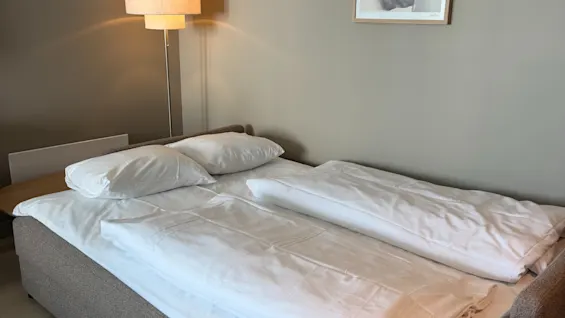 A cozy hotel room with a made bed, a warm lamp, and a framed picture on the wall, creating an inviting atmosphere.