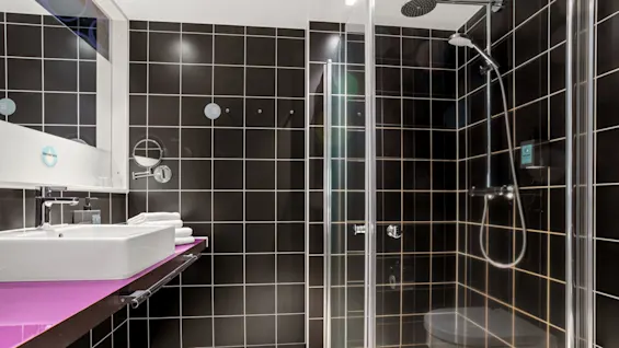 A modern bathroom with black tiles, white sink on purple countertop, and glass shower enclosure.