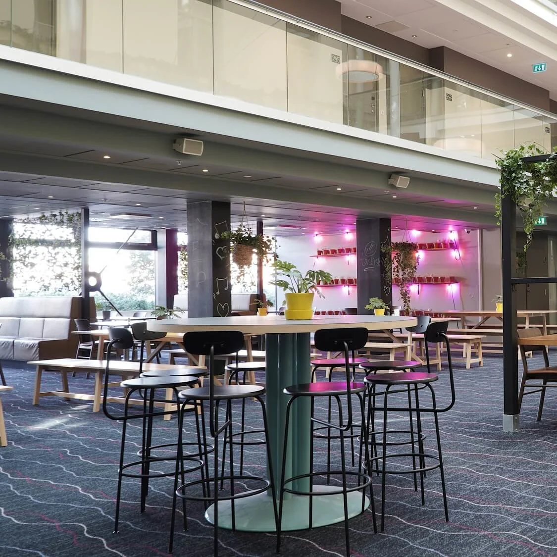 Modern interior with various seating areas, lit by pendant lights and natural light, in a spacious atrium with multi-level balconies.