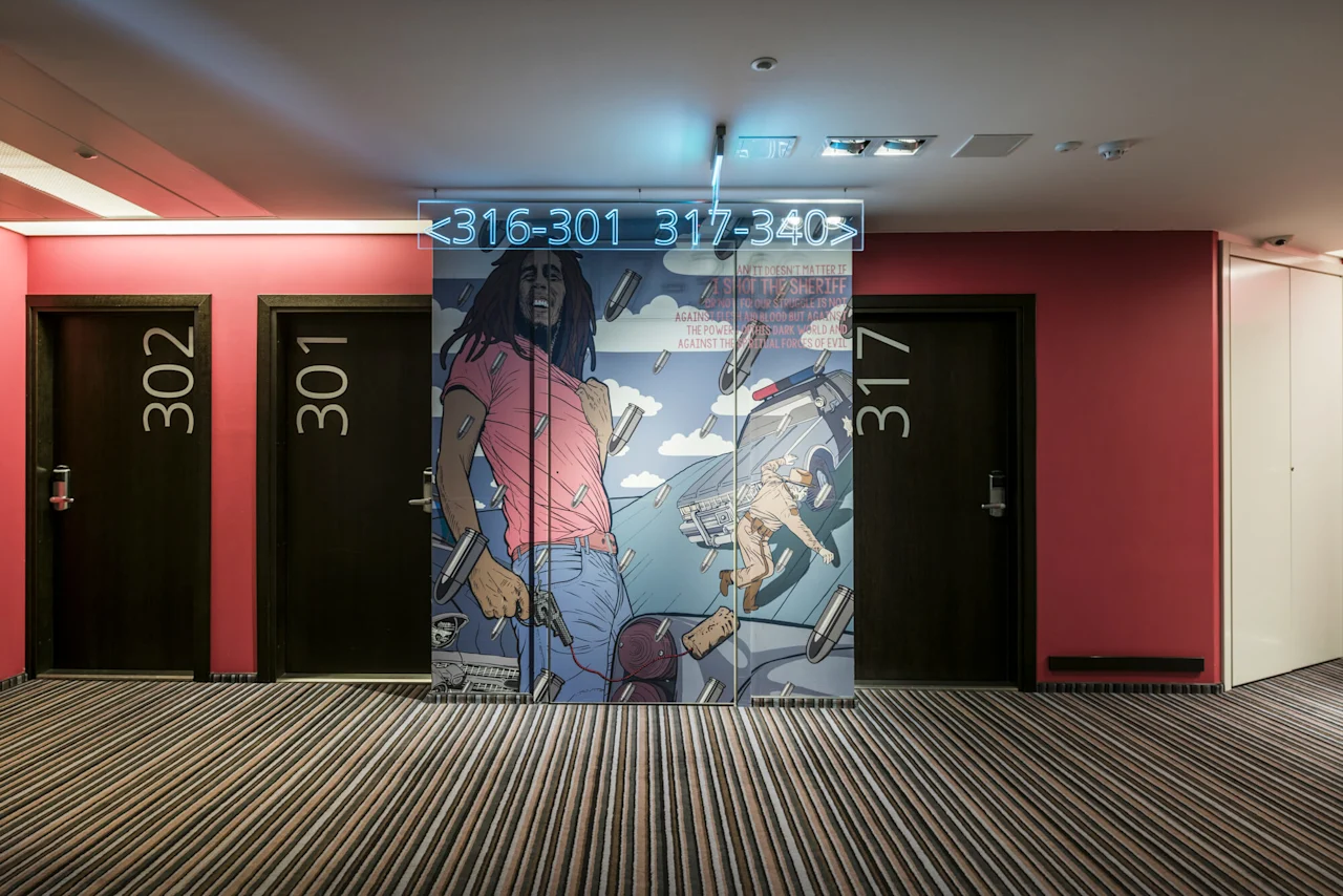 301 and 302 doors flank a mural of a person in a pink shirt with bullets. Striped carpet lines the floor. 