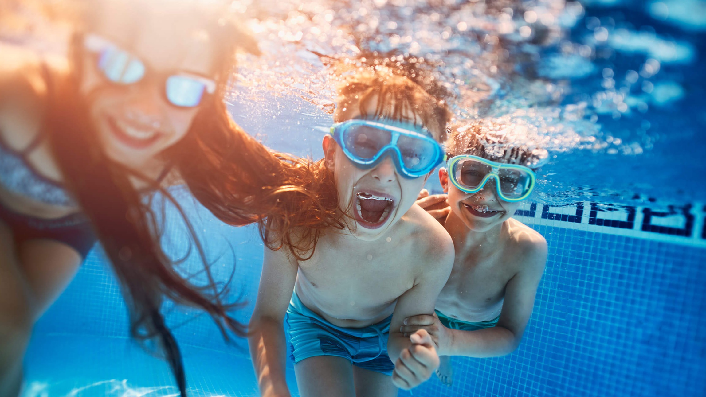 Børn med dykkermasker leger under vandet i en pool.