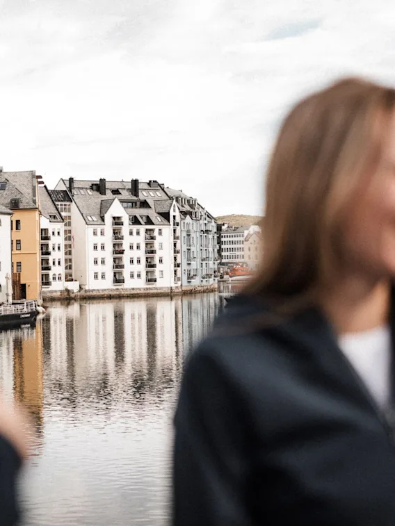 A person smiling by the water in front of the beautiful Art Nouveau buildings in Ålesund, Norway.