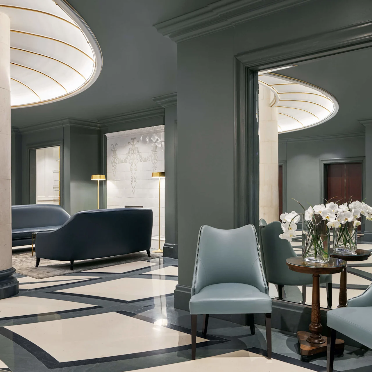Elegant lobby with blue sofas, chairs around a wooden table, flowers, under soft lighting, marble flooring at Hotel Kämp in Helsinki.
