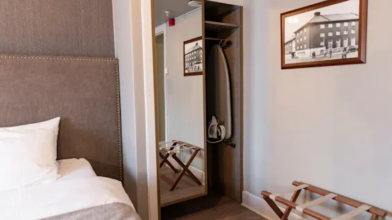 A cozy hotel room at Home Hotel Grand Bodø, featuring a comfortable bed, a mirrored wardrobe with an iron, and luggage storage.