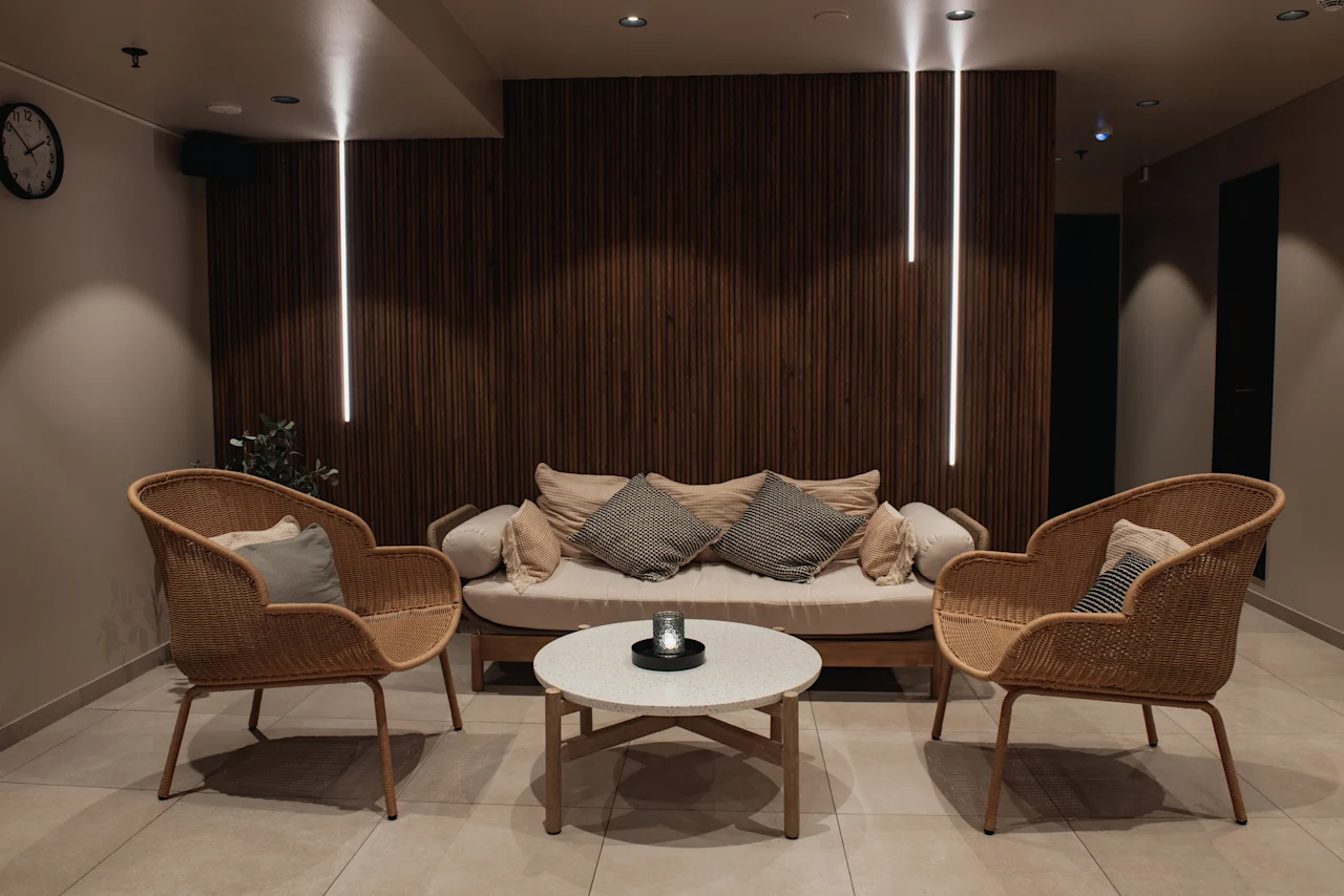 A cozy lounge area at Home Hotel Uppsala with a sofa, two armchairs, and a coffee table, featuring warm lighting and a wooden accent wall.