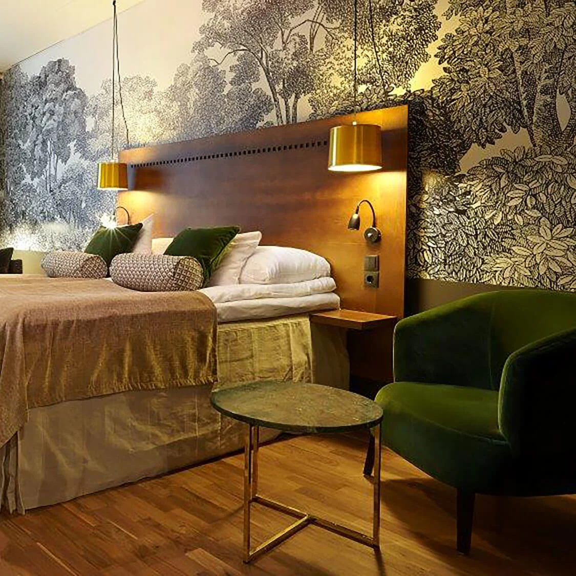A well-lit bedroom featuring a neatly made bed with pillows, flanked by elegant nightstands and a forest-themed wallpaper accent wall.