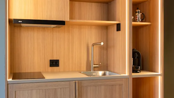 Modernt pentry med träskåp, diskho, spishäll och upplysta hyllor med kaffebryggare.