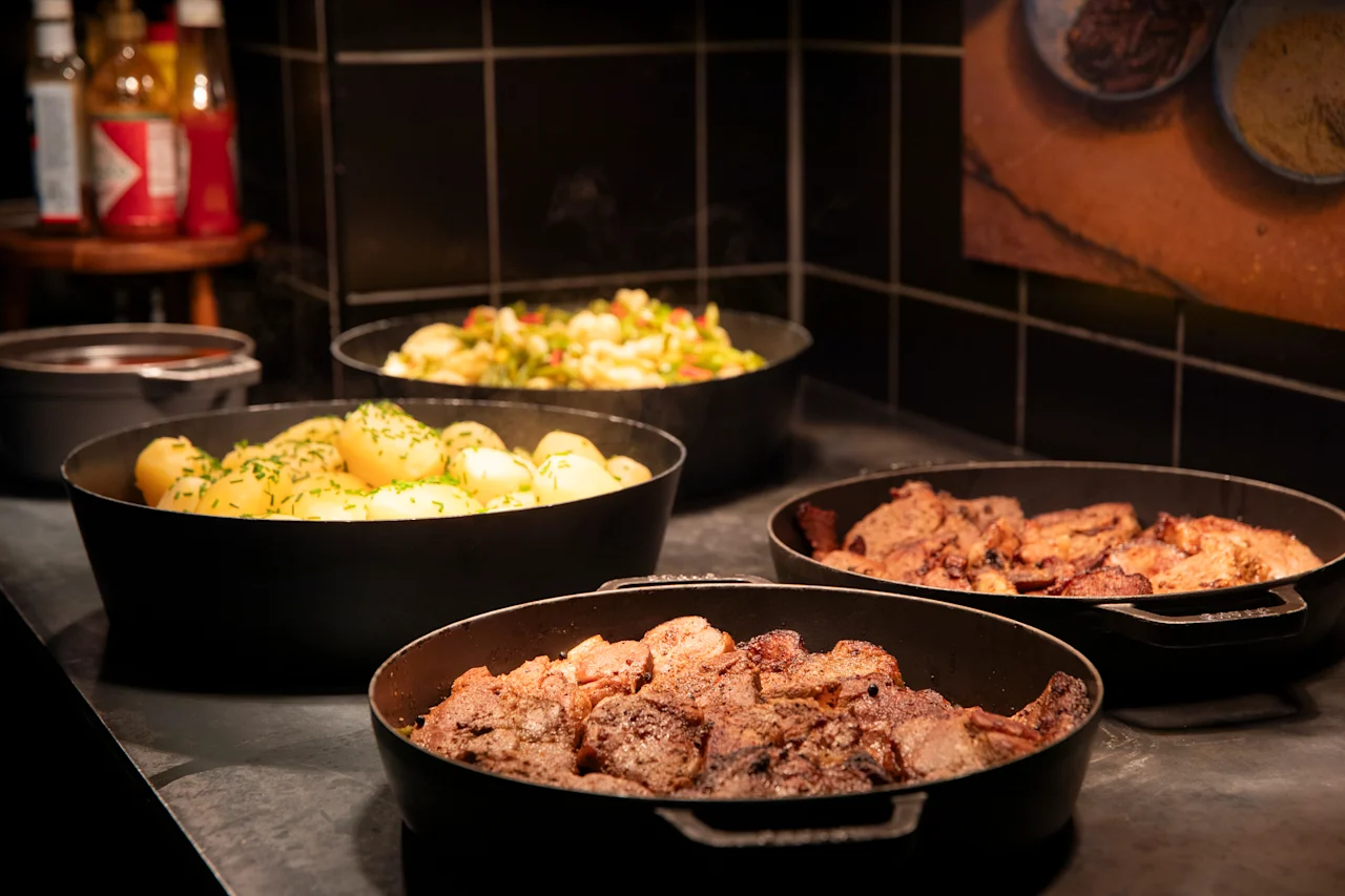 En deilig buffet med varme retter i svarte serveringsskåler, inkludert krydret poteter, blandede grønnsaker og smakfullt tilberedt kjøtt.