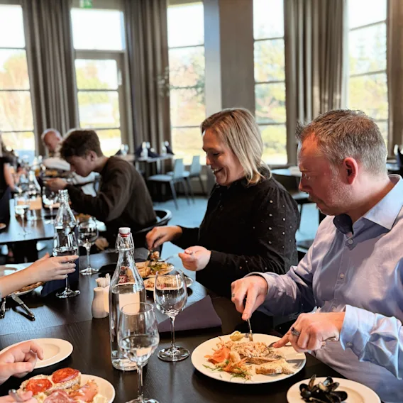 Folk som nyter et måltid sammen på en restaurant, med store vinduer som slipper inn naturlig lys.