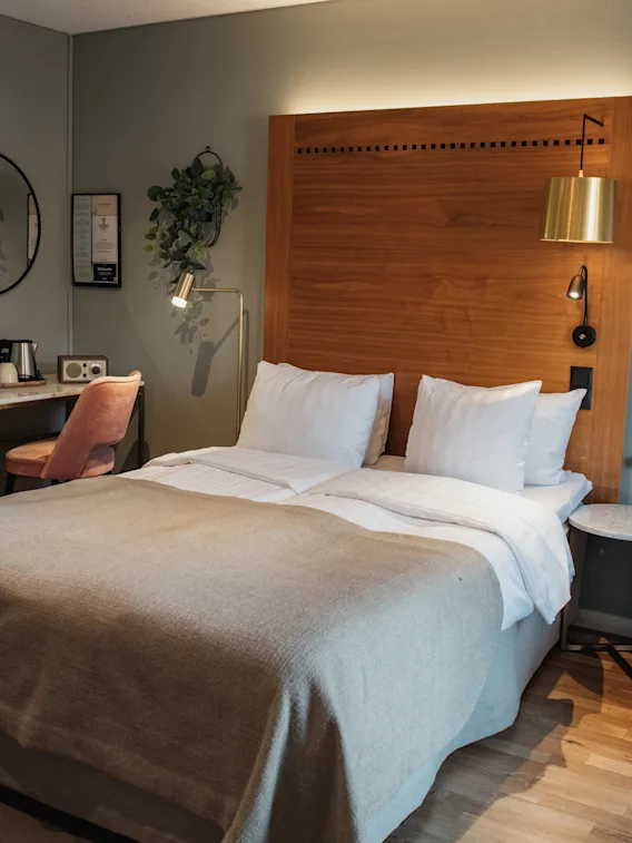 Ett välutrustat hotellrum med en stor säng, en skrivbordsplats med stol och en bekväm fåtölj, designat för avkoppling och produktivitet.