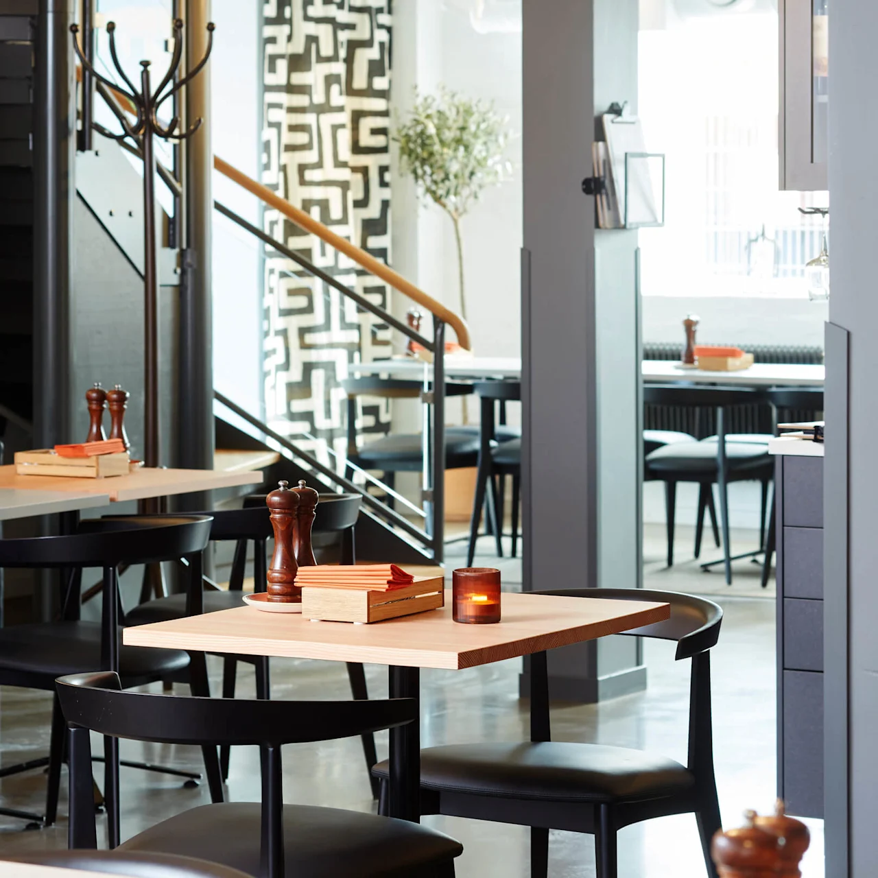 A dining area with a wooden table set with books, pepper mill, and a lit candle, inside a modern restaurant.