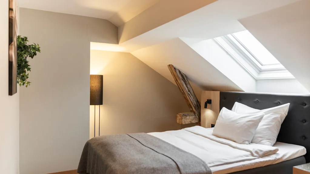 A cozy bedroom with a bed, a floor lamp, and a skylight in a room with sloped ceilings.