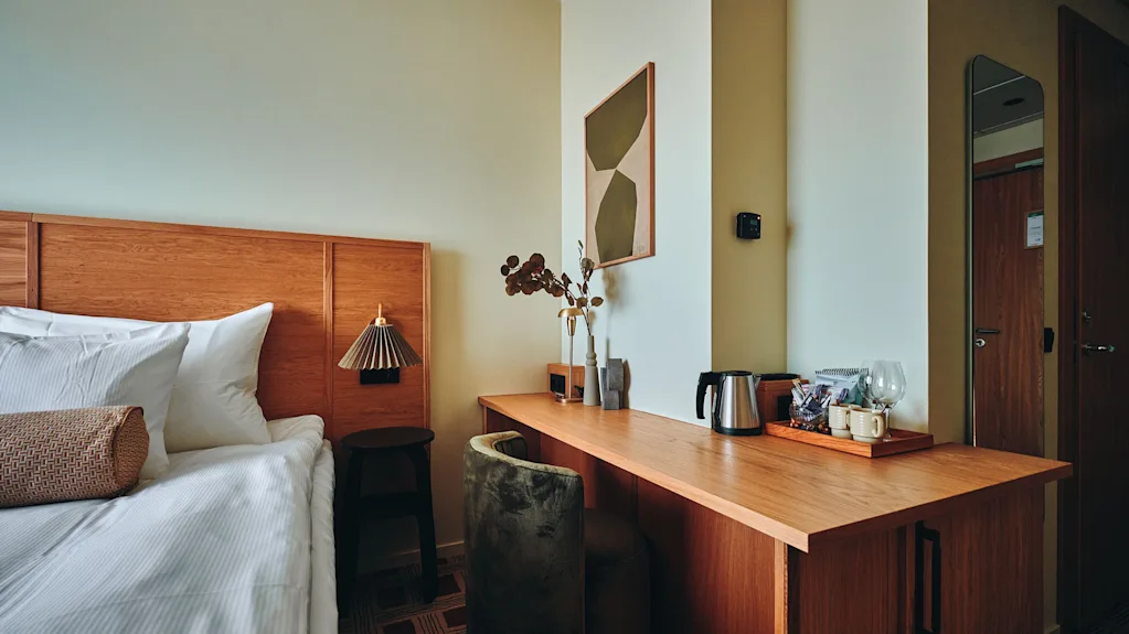 Et koselig hotellrom med en komfortabel seng, et treskrivebord med vannkoker og abstrakt kunst på veggen.