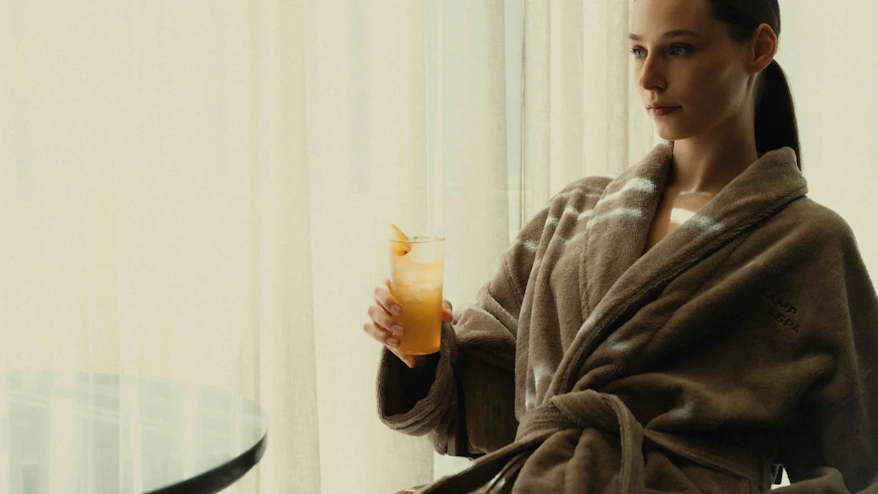 Person in a bathrobe enjoying a refreshing drink by a window, relaxing in a bright room.