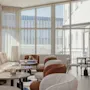 A bright and inviting lounge area with comfortable seating, small tables, and large windows looking out onto an urban scene.