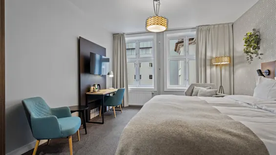 Ett modernt och inbjudande hotellrum med en bekväm säng, en funktionell skrivbordsplats och stora fönster som släpper in naturligt ljus.