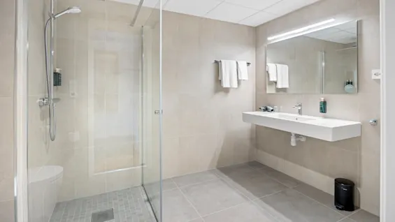 A modern bathroom with a walk-in shower, a long sink counter, mirrors, and tiled walls.