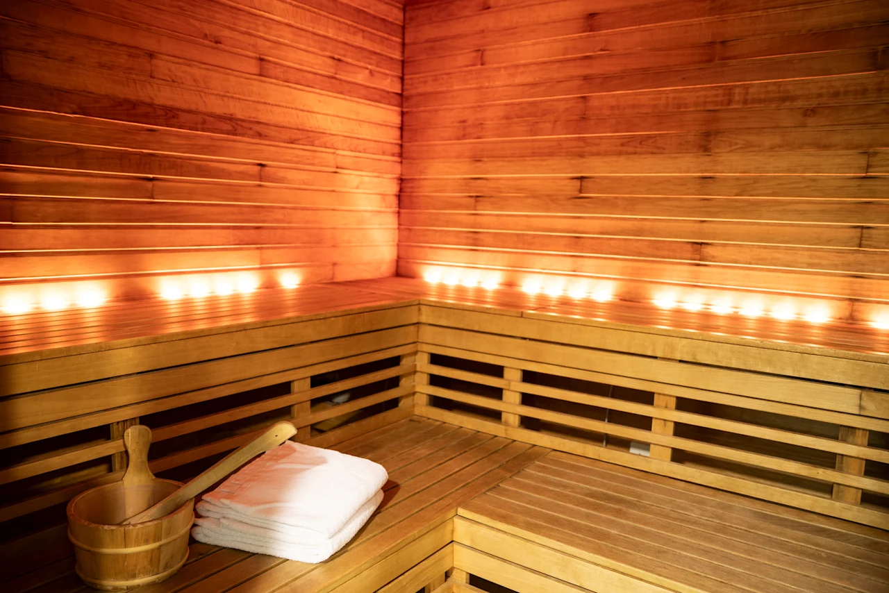 Interiör av en mysig träbastu med mjuk belysning, bänkar och tillbehör för en avkopplande upplevelse.