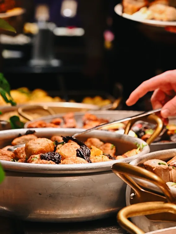 A person serving themselves food from a buffet, with various dishes in large pots.
