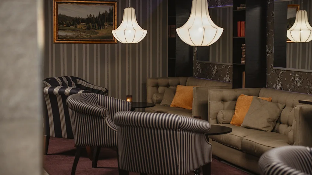Viihtyisä hotellin oleskelutila, jossa on raidallisia nojatuoleja, mukava sohva ja tyylikkäitä riippuvalaisimia, täydellinen rentoutumiseen.