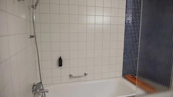 A clean and modern bathroom at Home Hotel Uppsala featuring a bathtub with a shower and white and blue tiled walls.