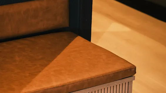 Close-up of a contemporary bench featuring a warm brown leather seat and a textured wooden design, with soft lighting.